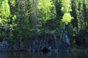 Jätturns naturreservat. En sjö i förgrunden med en brant klippvägg som går ner i vattnet. En grotta finns bergväggen. Grönskande skog ovanpå klippan.
