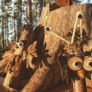 Små troll av pinnar och kottar vid en stubbe.
