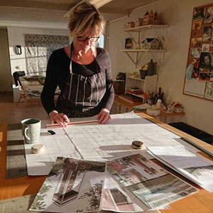 Kvinna står vid ett arbetsbord med stora ritningar och fotografier på det gamla utsiktstornet.