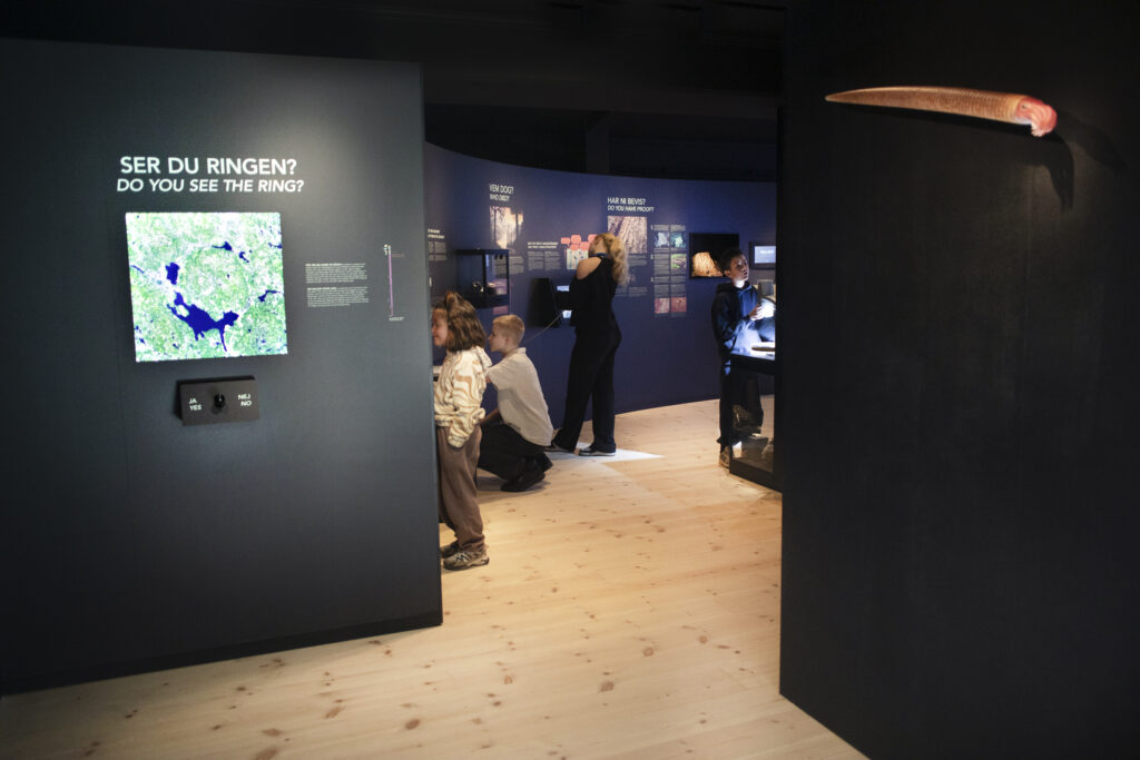 Bild på ingången till utställningen I meteoritens spår med svarta väggar och personer som interagerar med utställningen.
