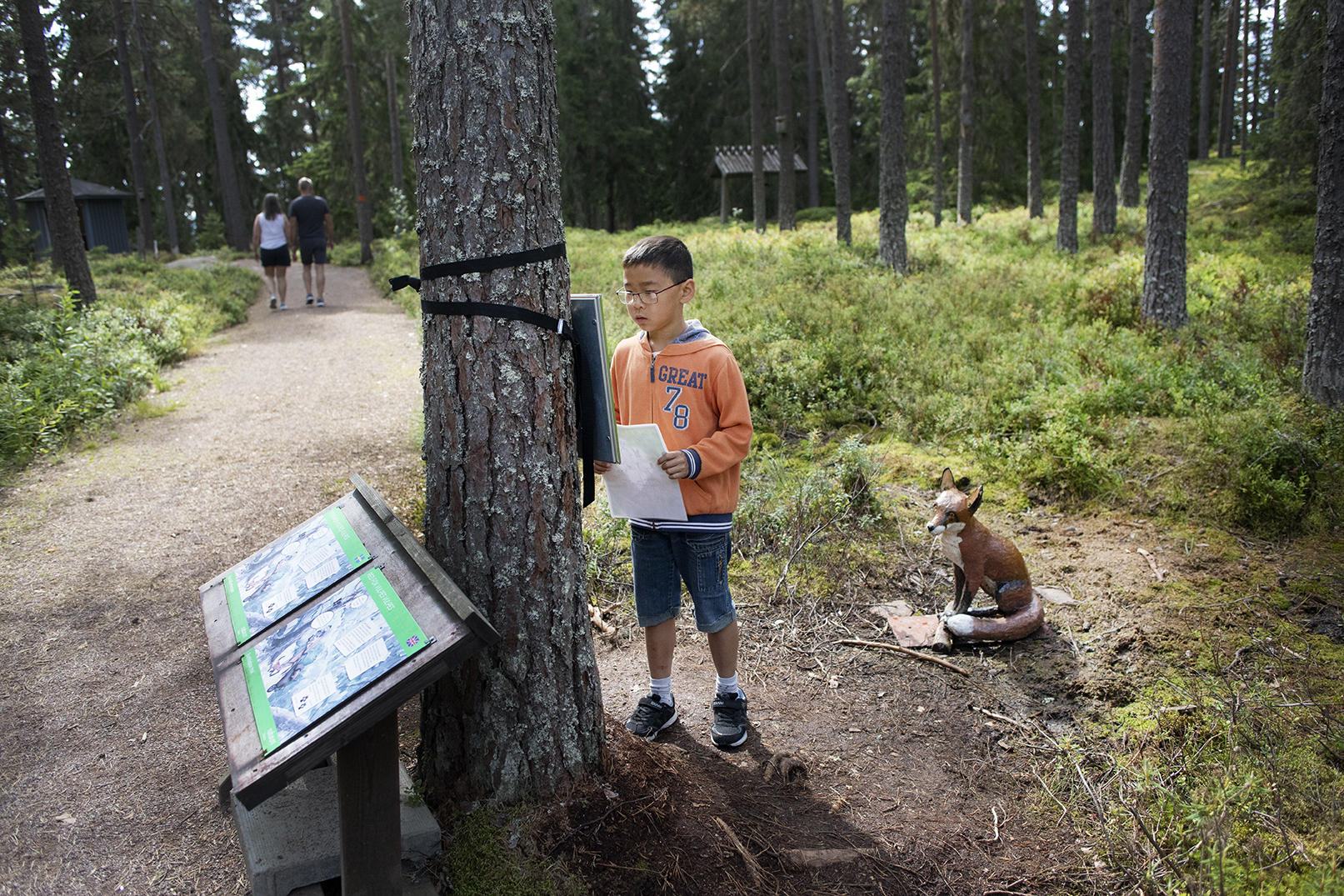 En pojke med svart hår och glasögon läser en fråga till skattjakten utanför naturum.