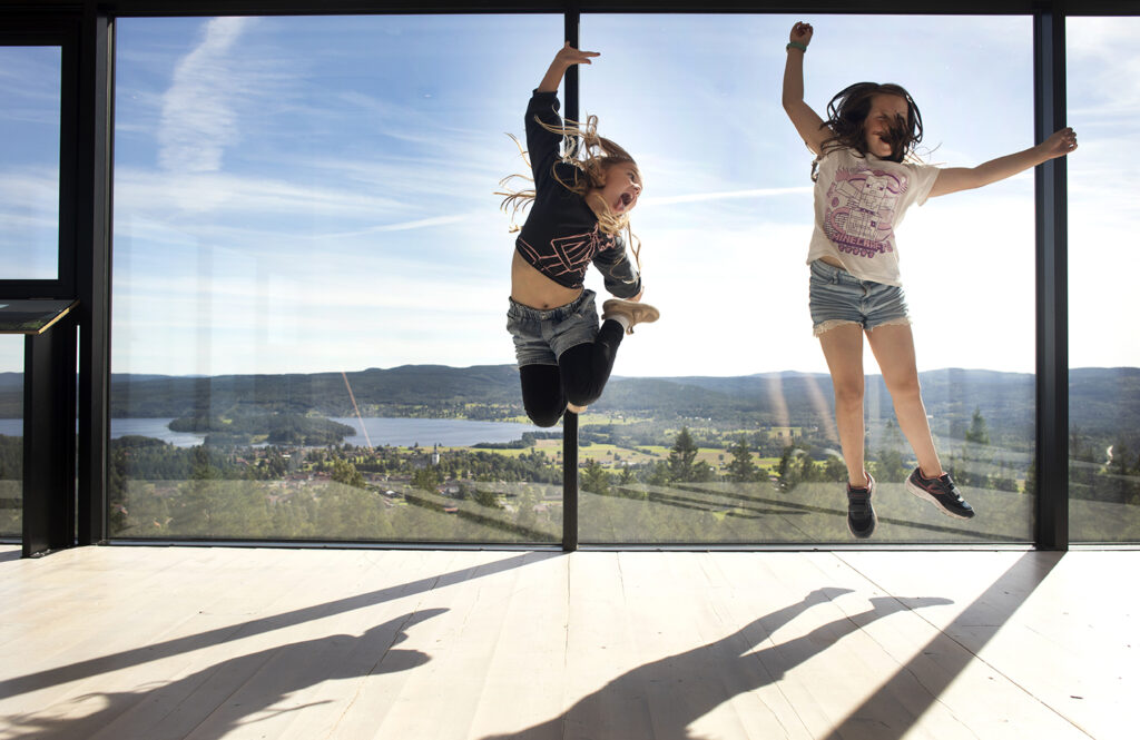 Två flickor hoppar glatt i det inglasade utsiktsdäcket på utsiktstornet.