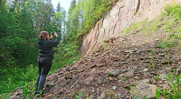 En kvinna fotograferar en bergsvägg i Amtjärnsbrottet.