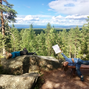 Två glada barn som ligger på en av utkiksplatserna. Det ena barnet sträcker upp skattkartan i vädret.