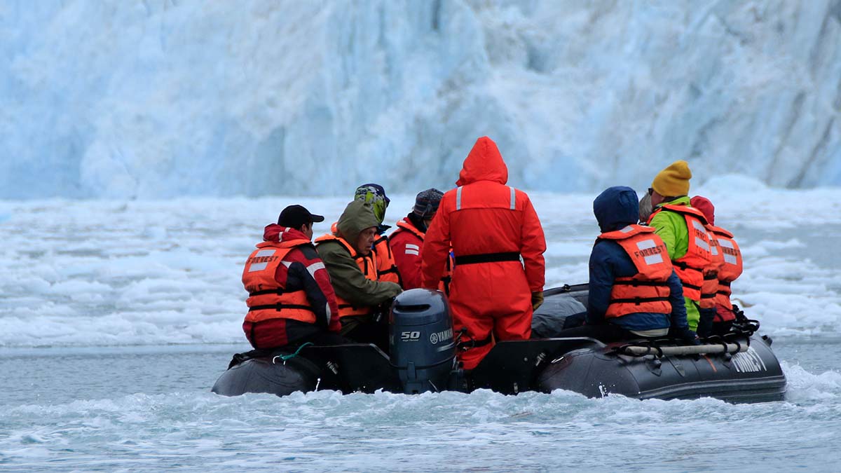 En grupp människor iklädda flytväst och varma kläder sitter i en gummibåt omgivna av isvatten och isberg i Chile.