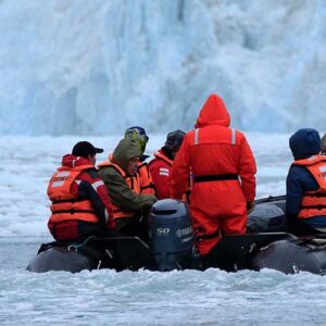 En grupp människor iklädda flytväst och varma kläder sitter i en gummibåt omgivna av isvatten och isberg i södra Chile.