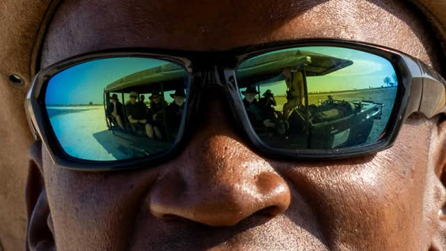 Närbild på en manlig safariguide i solglasögon i Botswana. I glasögonen speglas en jeep.