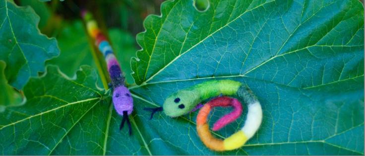 Två färgglada tovade ormar i ull ligger på ett rabarberblad.