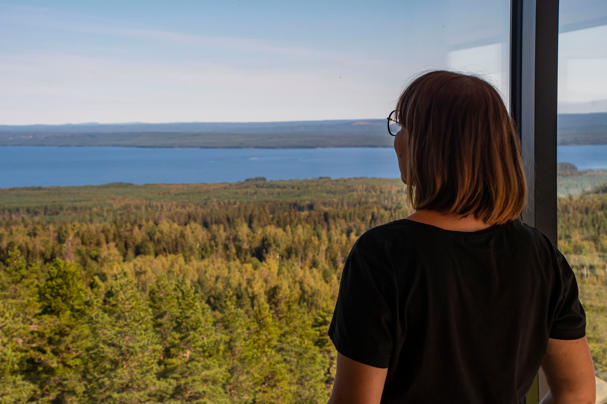 Kvinna med glasögon tittar stilla ut över Siljan från utsiktstornets innedäck.