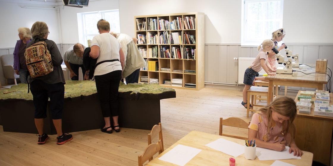 I biblioteket står en grupp pensionärer och tittar på landskapsmodellen över Dalarna, en flicka sitter och ritar och två barn tittar i stereolupparna i forskarhörnan.